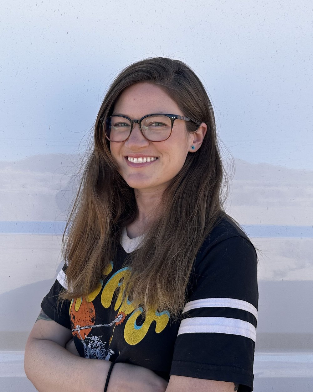 Tee, smiling, arms folded, standing against the side of her van